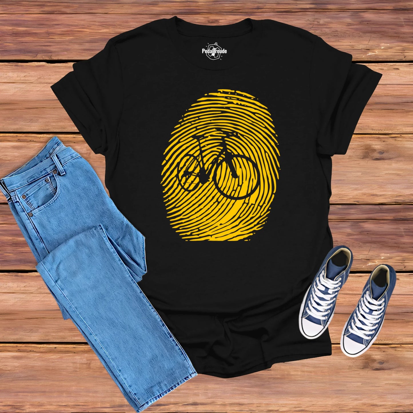 Hero Mockup eines schwarzen T-Shirts mit gelbem Fingerabdruck und Fahrraddesign – präsentiert mit Jeans und Sneakers.