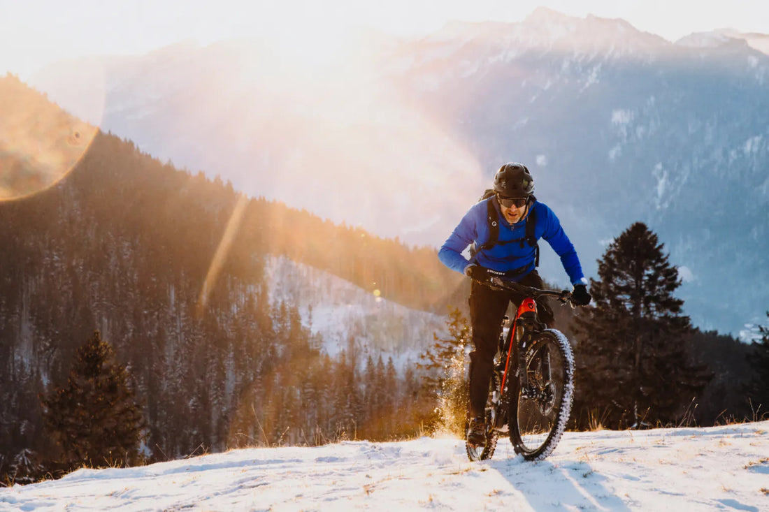 Cyclist riding a mountain bike through snowy alpine landscape at sunrise