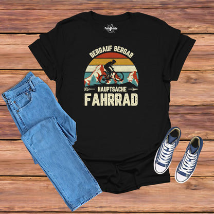 Schwarzes T-Shirt mit Vintage-Motiv eines Radfahrers in einer Berglandschaft. Der Text 'Bergauf Bergab, Hauptsache Fahrrad' ergänzt das design mit einer Retro-Farbpalette und einem Outdoor-Thema.