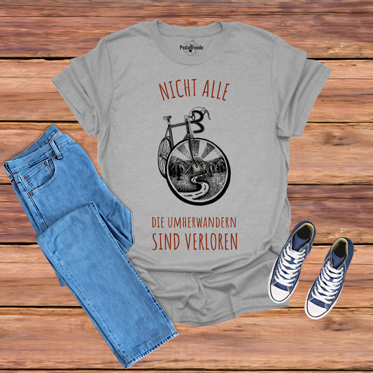 Graues T-Shirt mit einem kreativen Fahrraddesign. Das Motiv zeigt ein Fahrradrad mit Landschaftselementen wie Bergen, Sonnenstrahlen und einer Straße. Perfekt für Fahrradliebhaber und Abenteurer.
