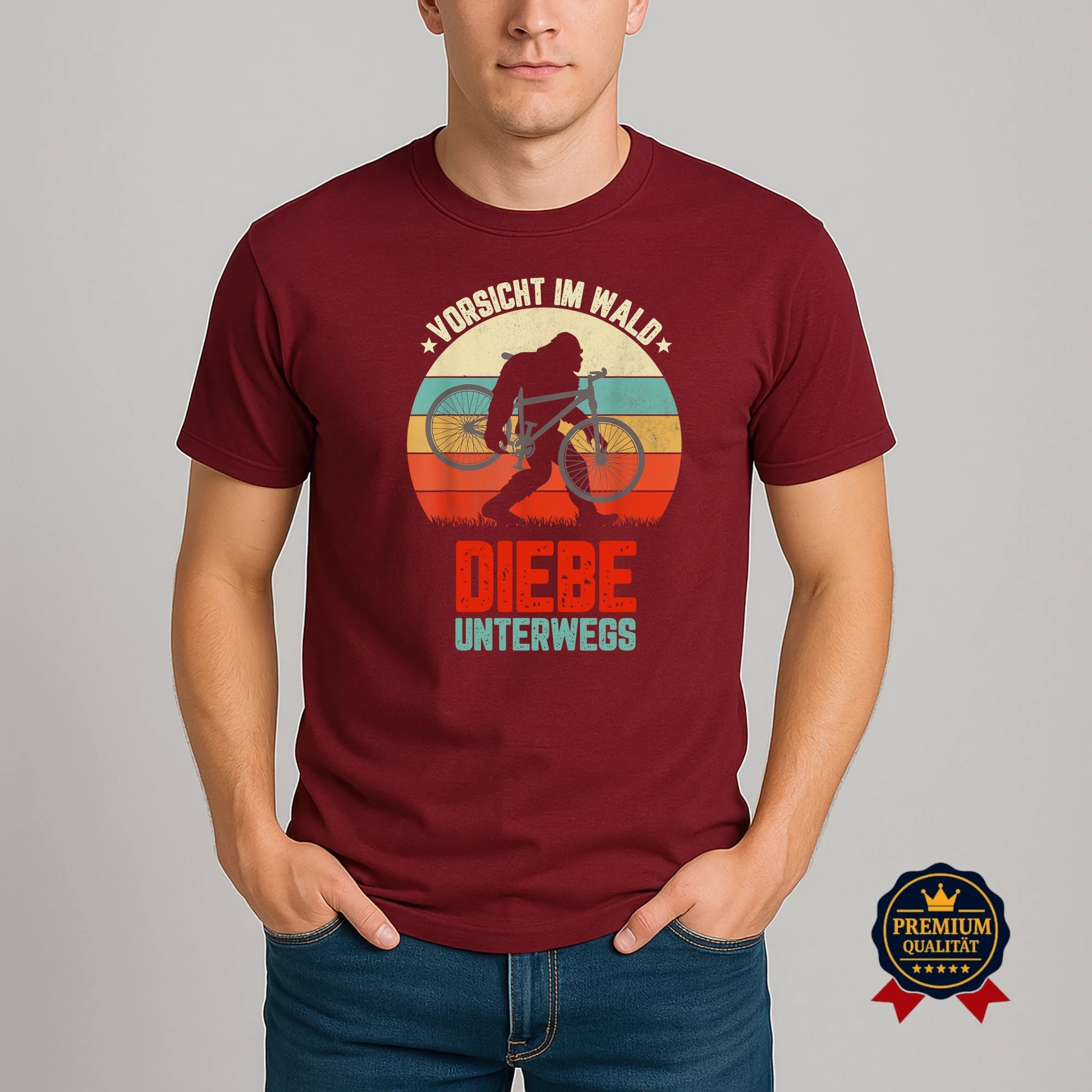 Model trägt burgundyfarbenes Fahrrad-T-Shirt mit Retro-Motiv ‚Vorsicht im Wald – Diebe unterwegs‘ und Bigfoot-Silhouette mit Fahrrad