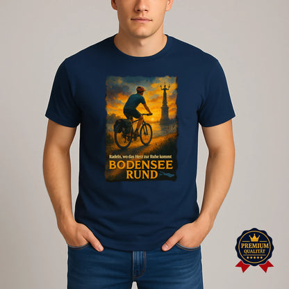 Mann trägt dunkelblaues Bodensee T-Shirt mit Radfahrer-Motiv bei Sonnenuntergang – Fahrrad Rundtour Design in Premium-Qualität