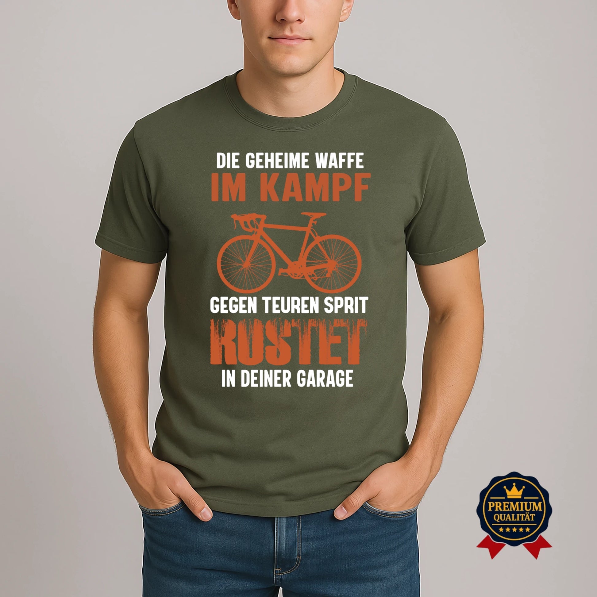 Olivgrünes Rundhals-T-Shirt mit Fahrrad-Design und humorvollem Statement 'Die geheime Waffe im Kampf gegen teuren Sprit – rostet in deiner Garage', getragen von Model.