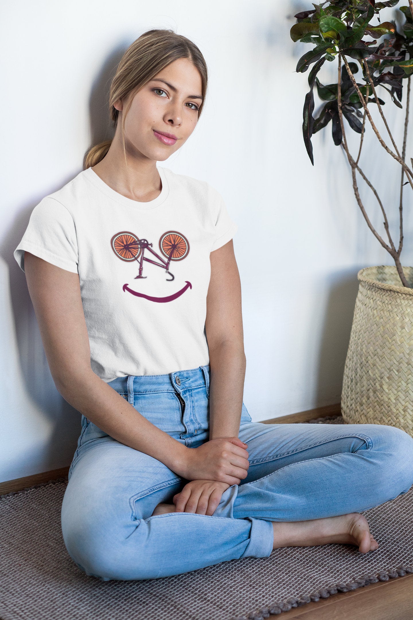 Frau sitzt barfuß am Boden mit weißem T-Shirt im Fahrrad-Smiley-Design – entspannter Lifestyle-Moment für Fahrradliebhaberinnen mit Herz